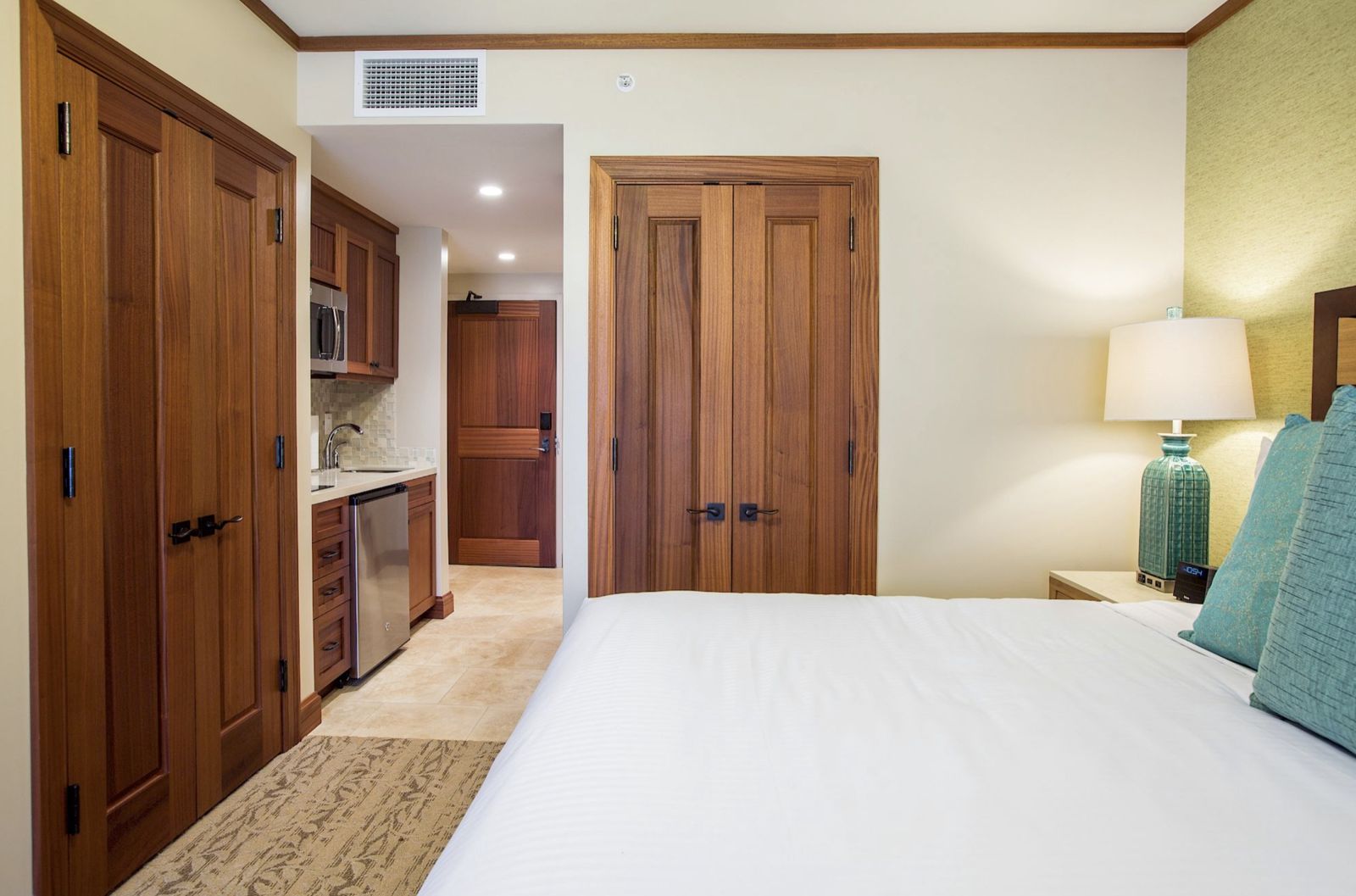Casita suite with a kitchenette, warm wood cabinetry, and a white-linen bed